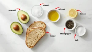 All ingredients for avocado toast laid out neatly: ripe avocado, sliced bread, lemon, salt, black pepper, and olive oil on a wooden table.