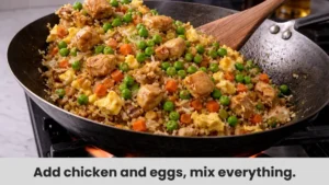Mixing chicken, eggs, and green onions into fried rice in a hot wok
