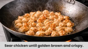 Chopped chicken pieces sizzling and browning in a hot wok with oil