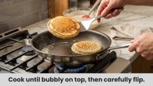 Pancake batter cooking in a hot non-stick pan with bubbles forming on the surface.