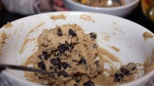 Stirring semi-sweet chocolate chips into cookie dough mixture with a spatula until evenly distributed