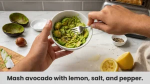 Hand mashing a ripe avocado with a fork in a small bowl, leaving some chunky texture