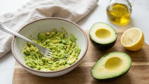 Hand mashing a ripe avocado with a fork in a small bowl, leaving some chunky texture