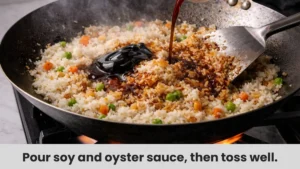 Soy sauce and oyster sauce poured over rice in a wok turning golden brown