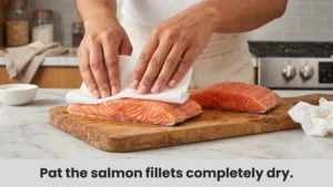 Raw salmon fillets being patted dry with paper towels before air frying.