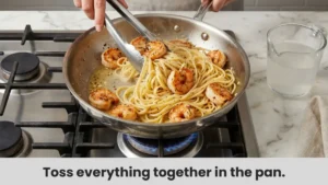 Chef tossing shrimp and linguine pasta together in a pan with sauce.
