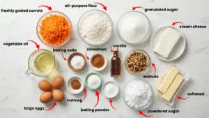 Carrot cake ingredients laid out on a marble countertop, including grated carrots, flour, sugar, oil, eggs, warm spices, walnuts, cream cheese, butter, and powdered sugar for the frosting.