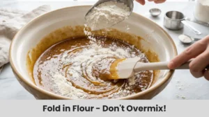 All-purpose flour being gently mixed into banana bread batter to avoid overmixing.