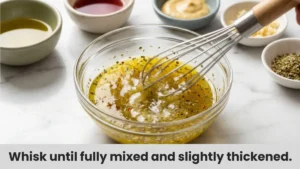 Whisking together olive oil, red wine vinegar, Dijon mustard, garlic, and oregano dressing for easy gluten-free pasta salad