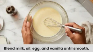 Smooth creamy wet mixture of milk, egg, oil, and vanilla extract whisked in a glass bowl for easy strawberry muffins.