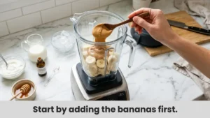 Adding banana slices, peanut butter, Greek yogurt, milk, vanilla extract, and honey into a blender to make a Peanut Butter Banana Smoothie.