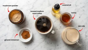 Easy mushroom coffee ingredients including mushroom powder, coffee beans, cinnamon, honey, and MCT oil on marble counter
