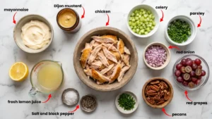 Fresh ingredients for summer chicken salad: grapes, celery, pecans, herbs, and rotisserie chicken on marble counter.