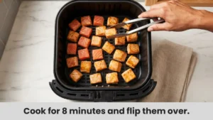 Air fryer salmon bites arranged in single layer in air fryer basket turning golden brown.