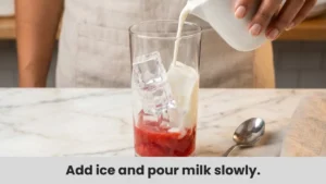 Step 2 for Starbucks strawberry matcha latte: ice cubes and cold milk poured over strawberry puree in glass.
