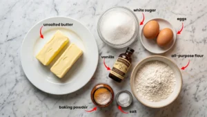 All ingredients for easy sugar cookie recipe: butter, sugar, eggs, vanilla, flour, baking powder, and salt on marble.