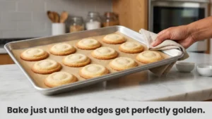 Step 8 of easy sugar cookie recipe: pulling a tray of golden-edged sugar cookies from the oven on parchment paper.