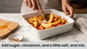 Mixing fresh peach slices with sugar and cinnamon for peach crisp filling in white baking dish